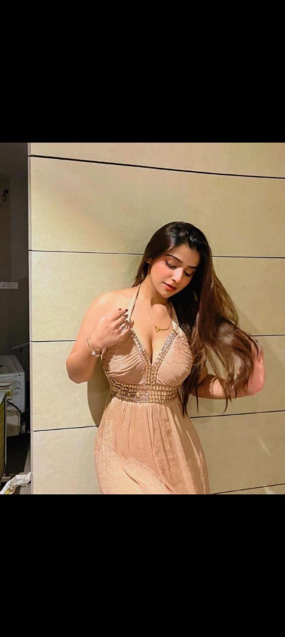 Woman with long brown hair in a beaded champagne halter dress posing against a wall.