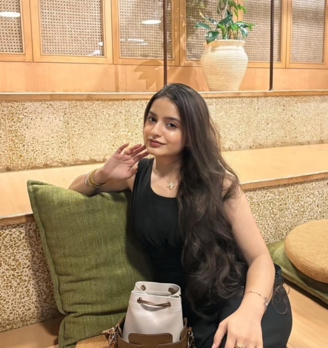 Young woman with long wavy hair sits on a bench against a green pillow.