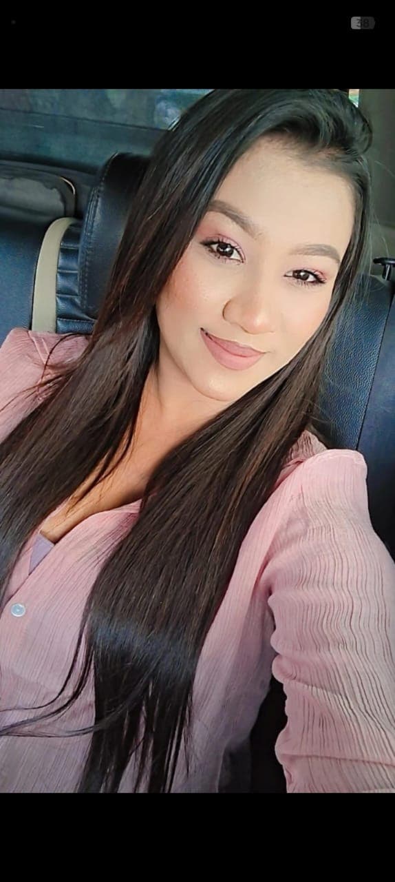 Smiling woman with long dark hair wearing a pink textured shirt inside a car.