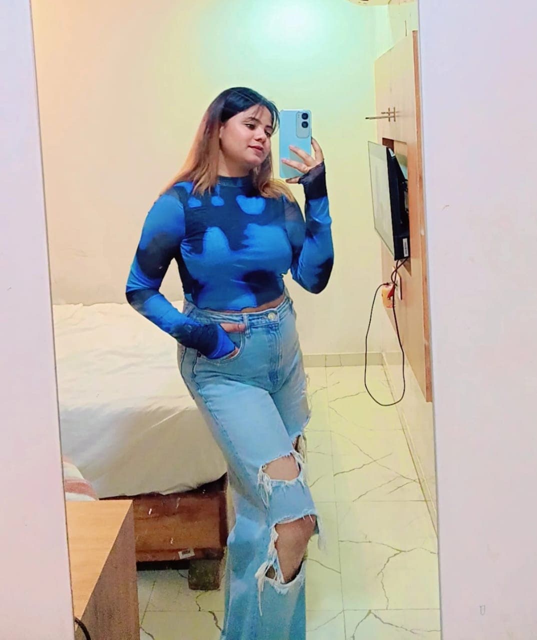 Woman taking a mirror selfie wearing a blue tie-dye top and light-wash ripped jeans.