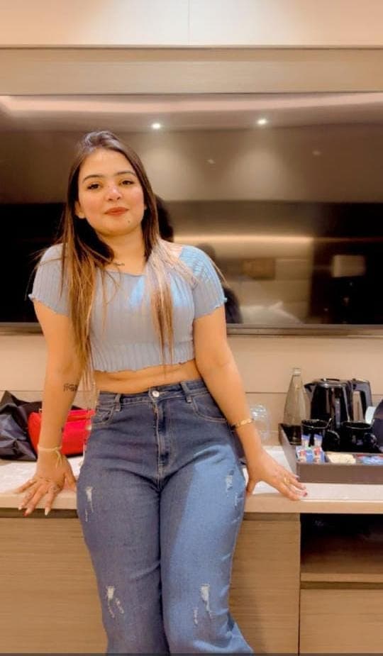 Long-haired woman in a blue crop top and distressed jeans leaning against a counter.